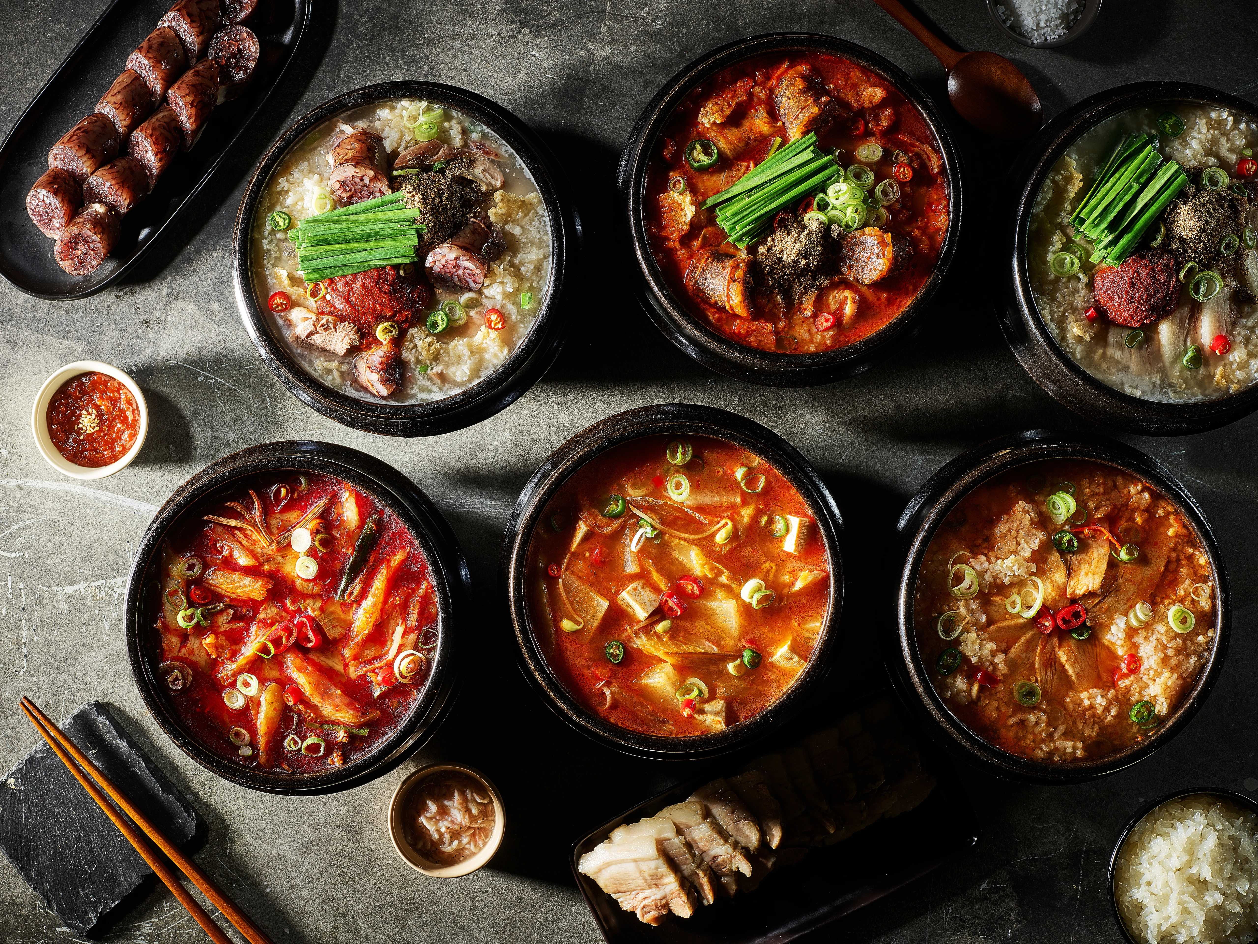 석재 테이블 위에 놓인 여섯 가지 국밥과 순대, 수육 한 상